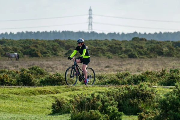 骑自行车的人骑着自行车沿着开阔的乡间道路骑着 车后有树木和电线 — 图库照片