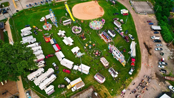 The bird\'s eye view of the amusement park on the green lawn surrounded by cars.