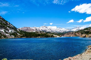 A natural view of a calm lake against snow-capped mountains in the background