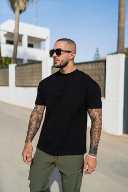 Siyah tişört ve yeşil pantolon giyen dövmeli genç bir adamın dikey fotoğrafı.