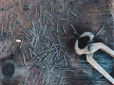 A pile of nails and rusty pliers on a weathered wood background