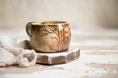 A closeup shot of an old ceramic mug on a wooden surface with a fabric on the side