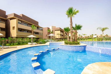 Palmiye ağaçları ve modern bir otel binası olan bir yüzme havuzu.