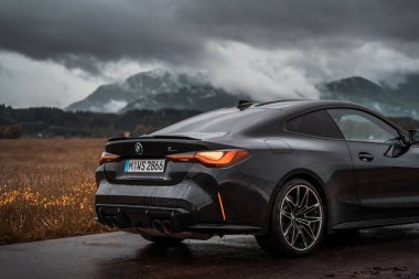 Dağlardaki modern bir BMW M4 'ün arka görüntüsü. Lüks spor araba birçok sürücünün rüya arabasıdır. Karanlık karamsar atmosfer