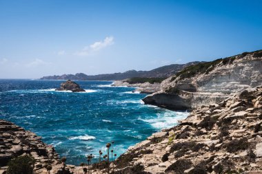 A beautiful shot of calm waves crashing on rocks on Corsica island on a sunny day