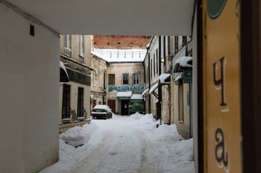 A beautiful shot of small tunnel covered with the snow and leading to old buildings and parked car