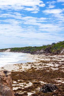 Bulutlu gökyüzü ve arka plandaki merdivenlerin altında bir sahil ve denizin dikey görüntüsü.