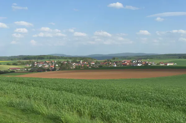 A natural view of a green field and village in the countryside under a cloudy sky