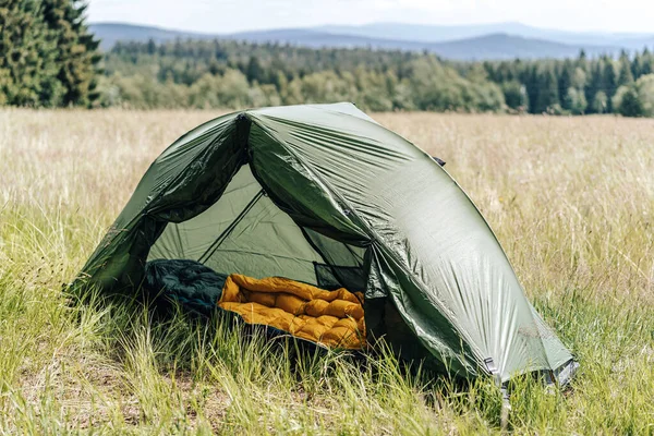 A green tent pitched on a high grass meadow. Opened tent in the mountains on a sunny day. Camping gear.