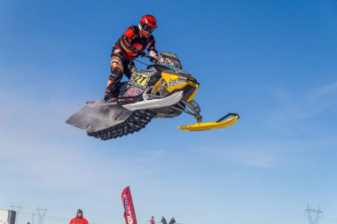 Kar arabası pistin üzerinden yükseğe zıplıyor. Kar motosikletinde, sporcuydu. Kış yarışması için bulutlu bir gün. Karda motorsporlar