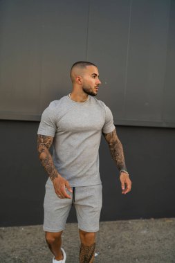 Aynı tişörtü ve şortu giyen dövmeli genç bir adamın dikey fotoğrafı.