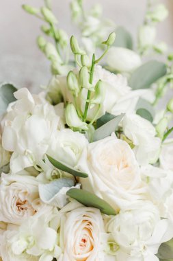 A vertical closeup of a beautiful bouquet of white roses and peonies with green leaves