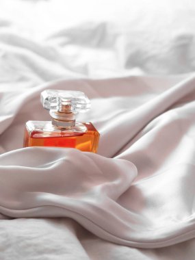 Beyaz bir kumaş arasında lüks bir kadın parfümü şişesinin dikey çekimi.