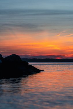A vertical shot of a bright sunset sky over a sea with rocks