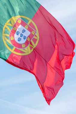 A vertical closeup shot of the waving flag of Portugal against the blue sky