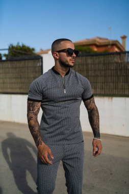 Aynı gömlek ve pantolona sahip genç ve dövmeli bir adamın dikey fotoğrafı.