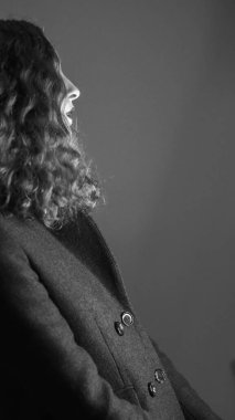 Gri bir duvara karşı poz veren şık elbiseli bir kızın yakın çekimi.