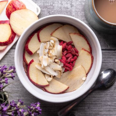 A flat lay of a breakfast bowl with apples, goji berries, and coconut flakes on a rustic table