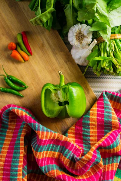 Capsicum cut on wooden cutting board with kitchen towel, red & green chillies, garlic and herbs selective focus photography shallow depth of field