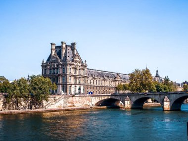 A scenic view of the Louvre Museum seen from the Seine River on a sunny day in Paris, France
