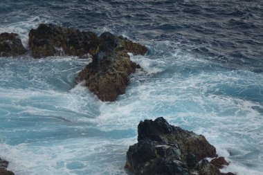 An overpass view of the ocean waves crashing over the rock formations at the cliffside of Flores island on a sunny day, Azores, Portugal