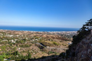 A panoramic view of fields and residential area in the shore of a sea under a clear cloudless sky