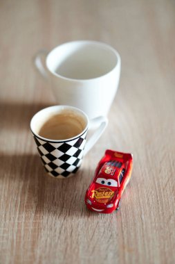 A vertical shallow focus of Lightning McQueen toy car next to cups of coffee on a table
