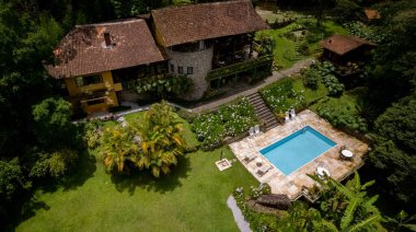 Panorama aerial showing empty lush tropical garden greenery with swimming pool on a mountain side with picturesque stone hotel exterior facade
