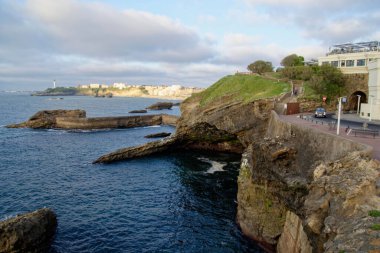 A beautiful view of a sea with huge rocks and an island under the cloudy sky