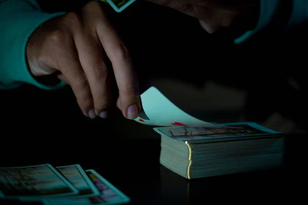 A man playing with cards on a table in a dark background