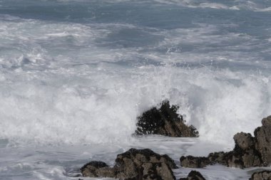 Büyük köpüklü dalgalar yazın güneşli bir gününde deniz kıyısındaki kayalara vuruyor.