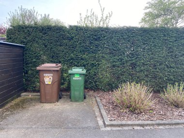 A view of brown and green trash cans near blooming bushes and plants