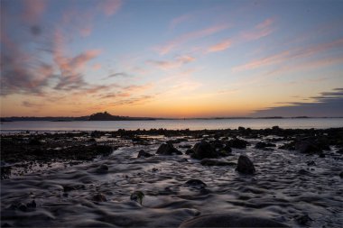 Kıyıdaki kayalara yakın çekim denizin üzerindeki güzel günbatımına karşı. Terenez, Fransa.