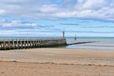 A beautiful view of a beach with a pier over the water under cloudy blue sky