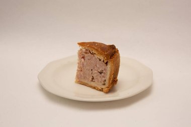 A tasty British crusty pork pie slice on a plate isolated on a white background