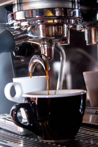 A vertical closeup shot of a coffee machine pouring coffee into a black cup