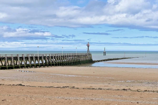 A beautiful view of a beach with a pier over the water under cloudy blue sky