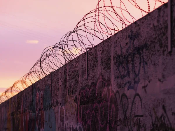 Gün Batımında Duvarın Tepesinde Grafiti Sanatlarıyla Çevrili Dikenli Tellerin Yakın — Stok fotoğraf