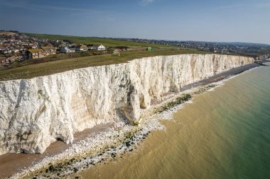Okyanusu ve arka planda küçük bir kasabası olan kumtaşı kayaları manzaralı bir sahil manzarası.