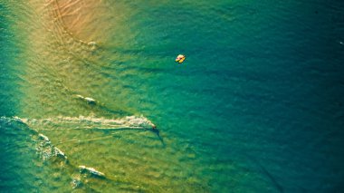 Okyanusun sığ turkuaz suyunun ve bir uçurtma sörfçüsünün hava aracı görüntüsü.