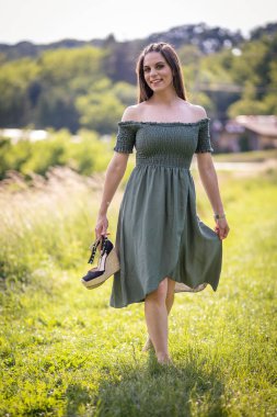 Güneşli bir günde çimlerin üzerinde duran yeşil elbiseli, beyaz bir kızın güzel bir fotoğrafı.