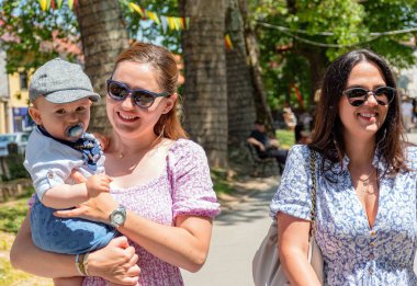 İki beyaz kadın ellerinde bebekle sokakta yürüyorlar.