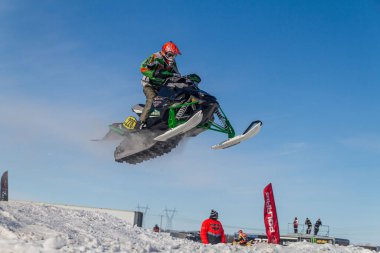 Kar arabası pistin üzerinden yükseğe zıplıyor. Kar motosikletinde, sporcuydu. Kış yarışması için bulutlu bir gün. Karda motorsporlar