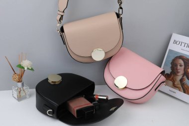 The women's bags full of cosmetics and aroma reed diffuser on a white table