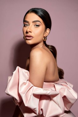 Pürüzsüz at kuyruklu, ladin rengi bir duvarın karşısında pofuduk bardot tarzı elbisesi olan beyaz bir kadın modelin portresi.