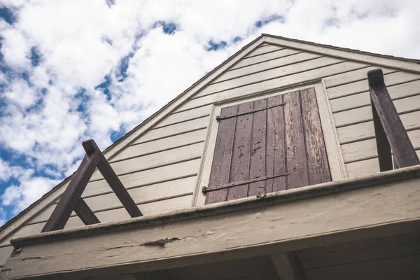A low-angle shot of an old wooden house against a blue cloudy sky