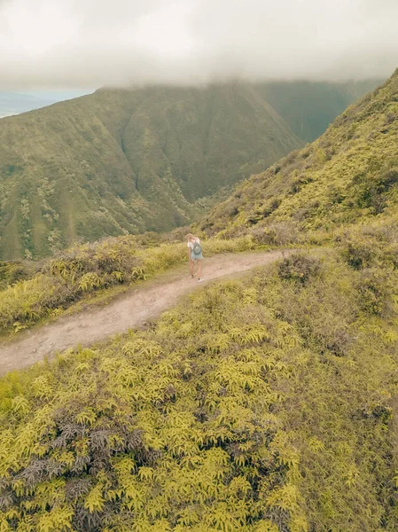 A bird\'s eye view of a female hiking the green mountains covered with clouds in Oahu, Hawaii