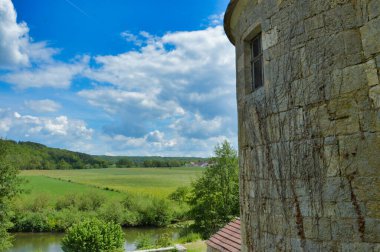 A ancient castle wall with a green field, forest and cloudy sky on the background
