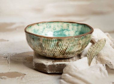 Ahşap bir yüzey üzerinde eski seramik mutfak eşyalarının yakın plan bir fotoğrafı ve yanında da kurumuş yaprak ve kumaş var.