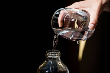 Bir elin yakın çekimi bardaktan suyu şişeye dolduruyor.